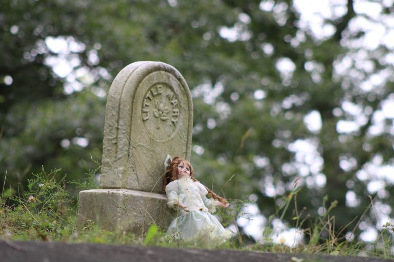 A porcelain doll placed on an old grave marker inscribed “Little Mary”.