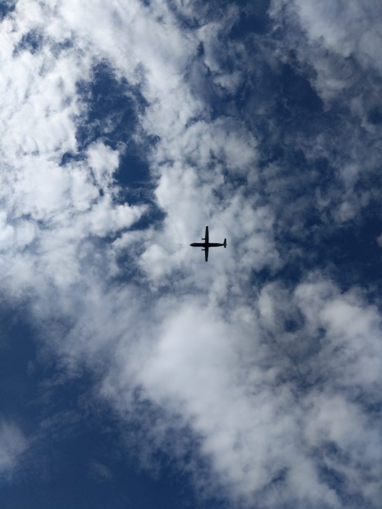 Silhouette of a two propeller aeroplane in flight taken amongst the mostly cloud filled sky.