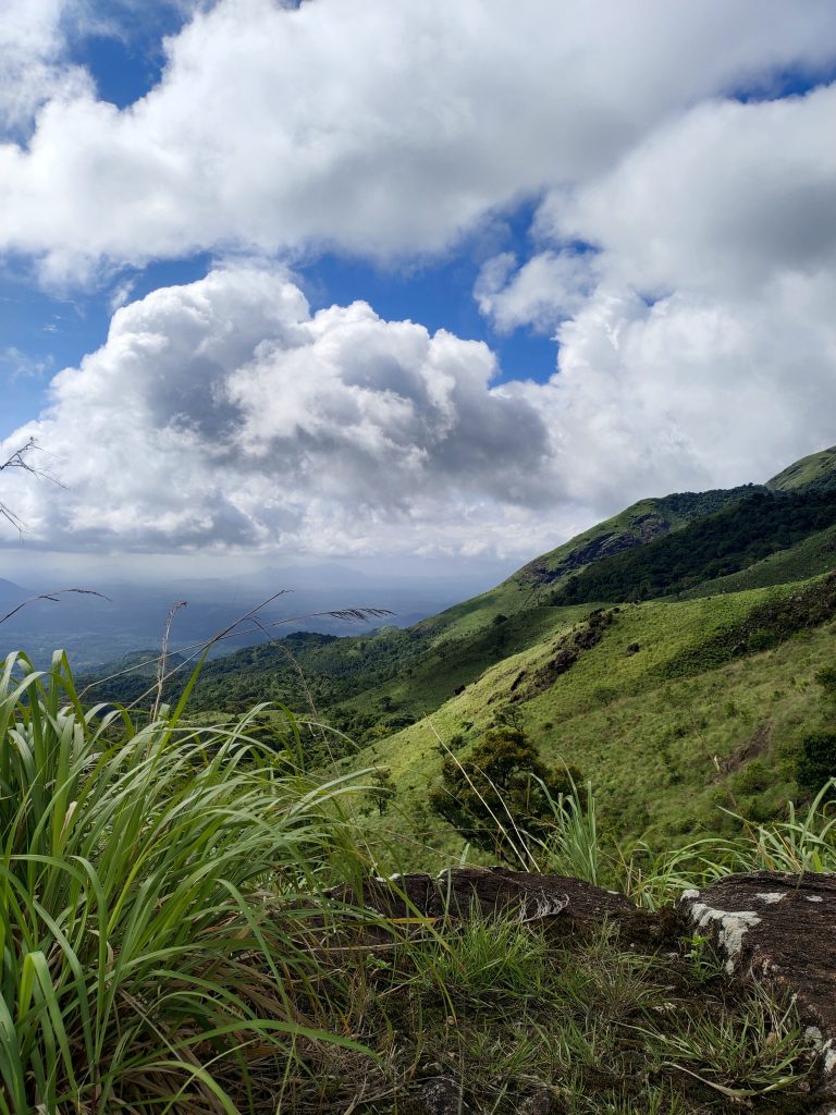 Long view of green mountains with puffy clouds in the sky. View from a mountain top.