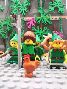 Miniature toy elf figures, a cow and a chicken fixed on a board, Lego style