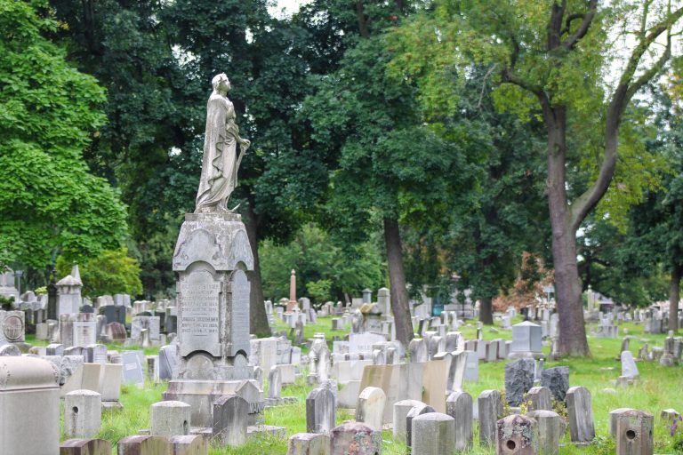 A statue of a woman looks to the sky atop a tall gravestone rises above a sea of old headstones at Mt. Hope Cemetery in Rochester, New York, USA.