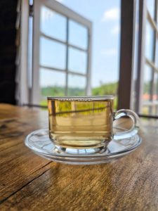 A Cup of white tea on a wooden table besides an open window. 
