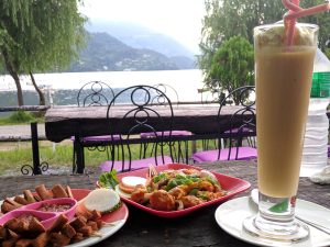 Common Nepali Food MoMo, Mango Lassi and Sussages on the table with background view of Phewa Lake and Mountains in Pokhara, Nepal
