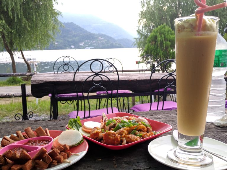 Common Nepali Food MoMo, Mango Lassi and Sussages on the table with background view of Phewa Lake and Mountains in Pokhara, Nepal