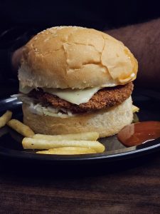 Closeup shot of chicken burger and chips with red sauce.