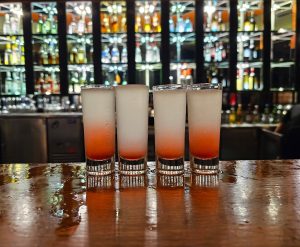 Picture of 4 glasses of shooters on a bar counter.
