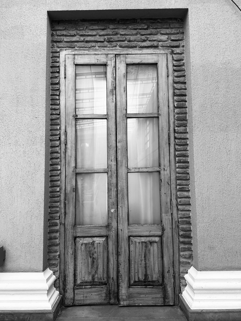 Old wooden door, with brickwork surround encased in concrete render with sculpted floor edging.