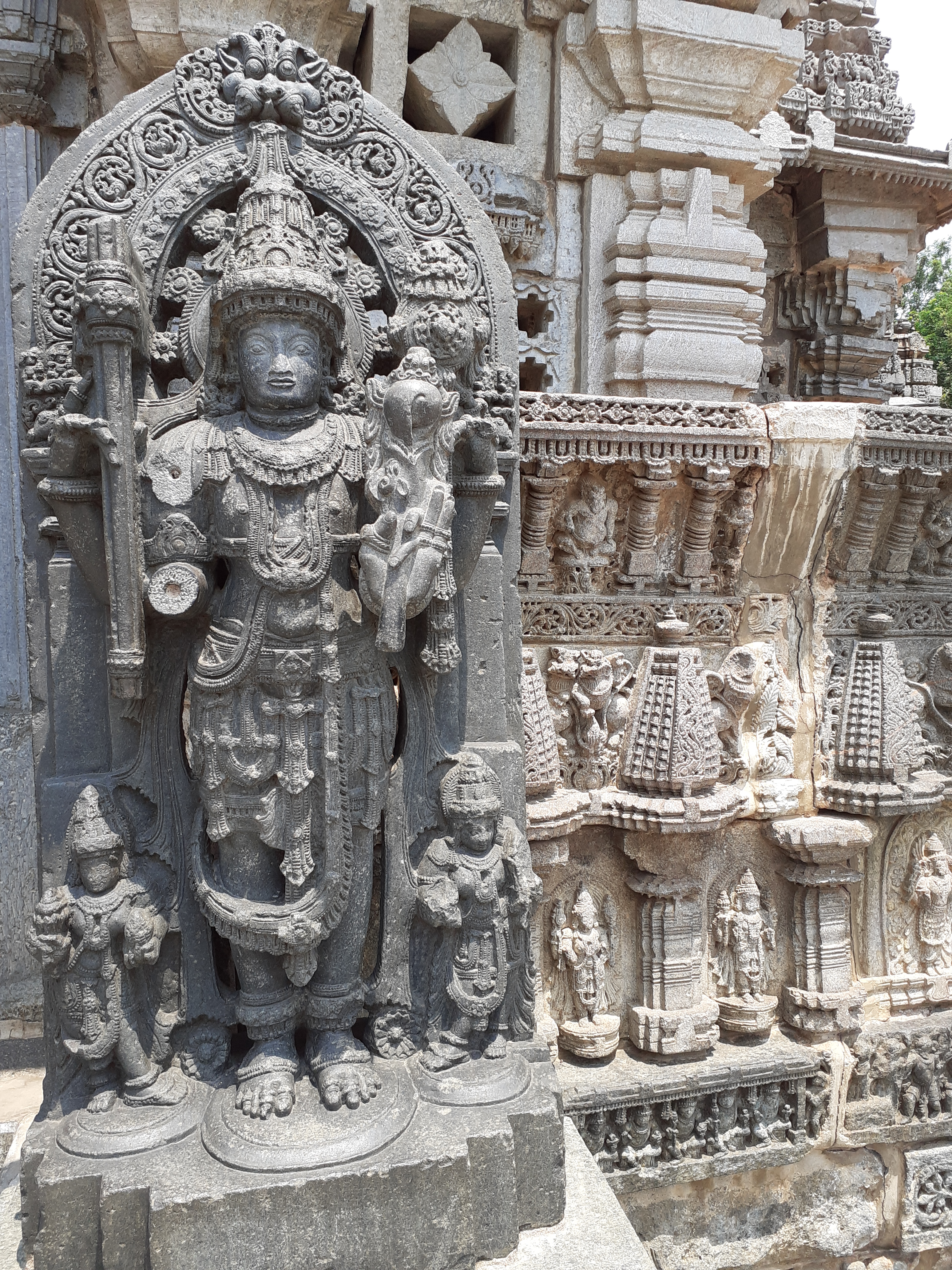 Ornate sculpture forming part of a building, possibly a temple with a tree to the right.