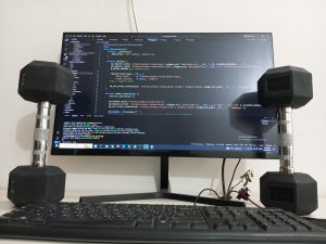 Dumbells rest upright on either side of a keyboard and computer monitor displaying code.
