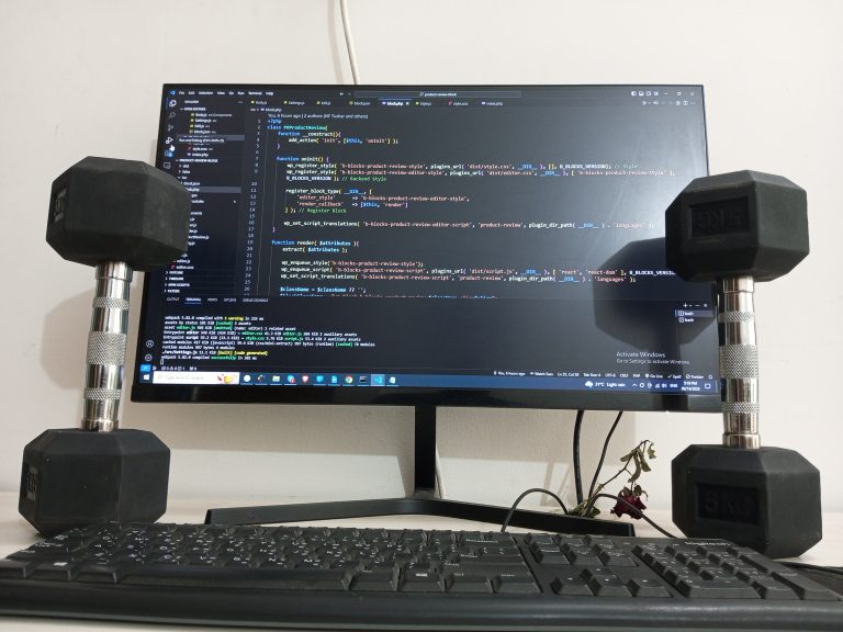 Dumbells rest upright on either side of a keyboard and computer monitor displaying code.