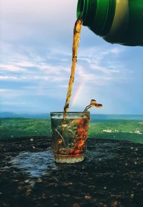 Beverage poured into a cup on a cloudy day in an open landscape with the backdrop of a beautiful rainbow 
