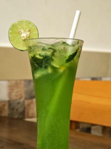 A glass of mojito with mint leaves and a lemon slice fixed on the top. 
