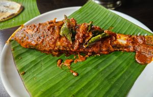 Kerala style tawa fried fish with special masala and curry leaves resting on a banana leaf 
