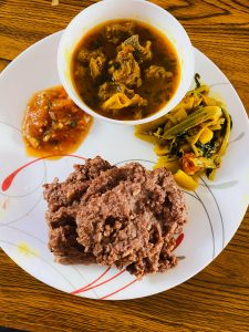 A bowl of soup sitting on a plate of vegetables, sauce and a Bhaji 