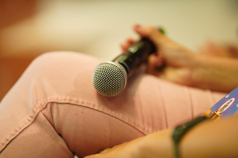 Hand holding a microphone on a lap while seated at WordCamp Pontevedra 2023