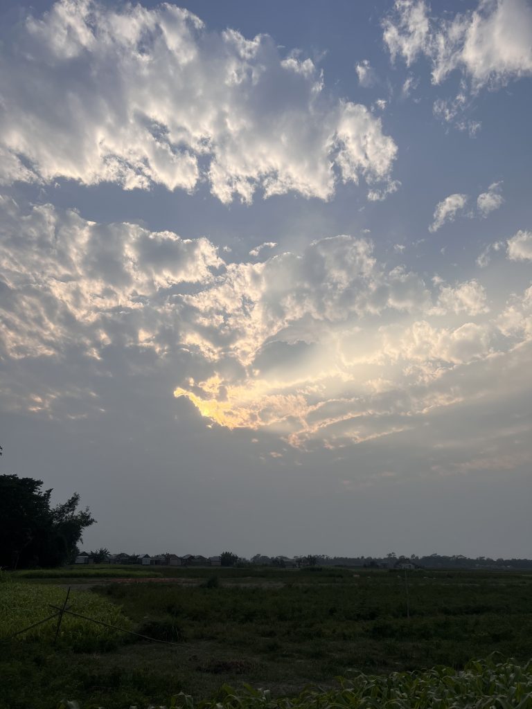 A Beautiful Before Rain Sky View With Clouds. The sun is beaming through a hole in the clouds, bright above an otherwise dim landscape.