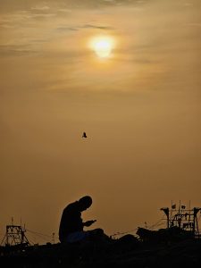 Glued to the screen! Silhouette of a man looking at his mobile during sunset on a harbor. 