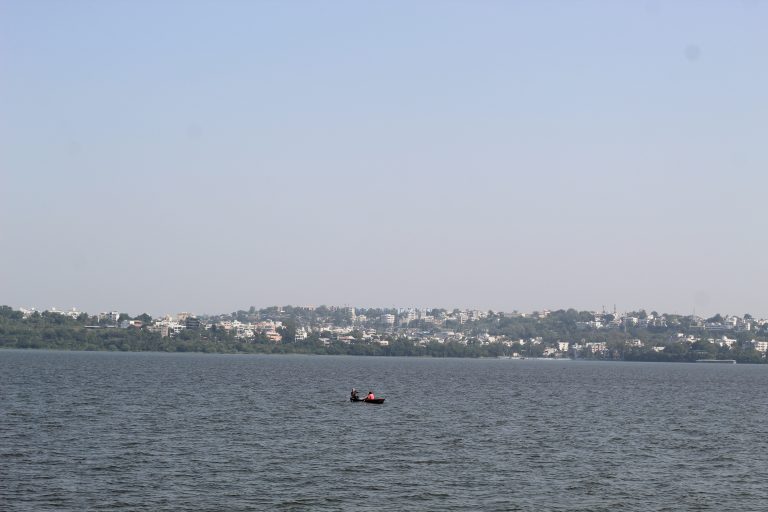 A city surrounded by lake and a boat in the middle of the lake.