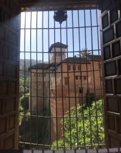 A look through a barred window towards one of the buildings in Alhambra standing on a hill

