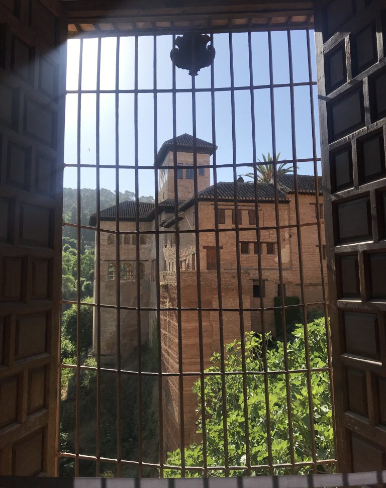 A look through a barred window towards one of the buildings in Alhambra standing on a hill