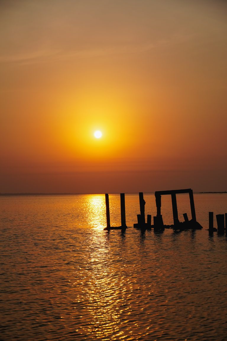 Golden hues embrace the horizon as the sun bids farewell, casting a warm glow over tranquil waters.