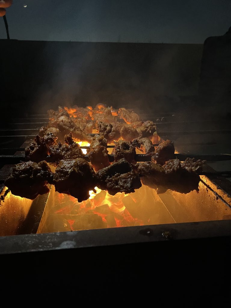 Flames and smoke engulfing chicken on a barbecue grill at night, creating a mouthwatering spectacle of cooking. (#WCBhopal)