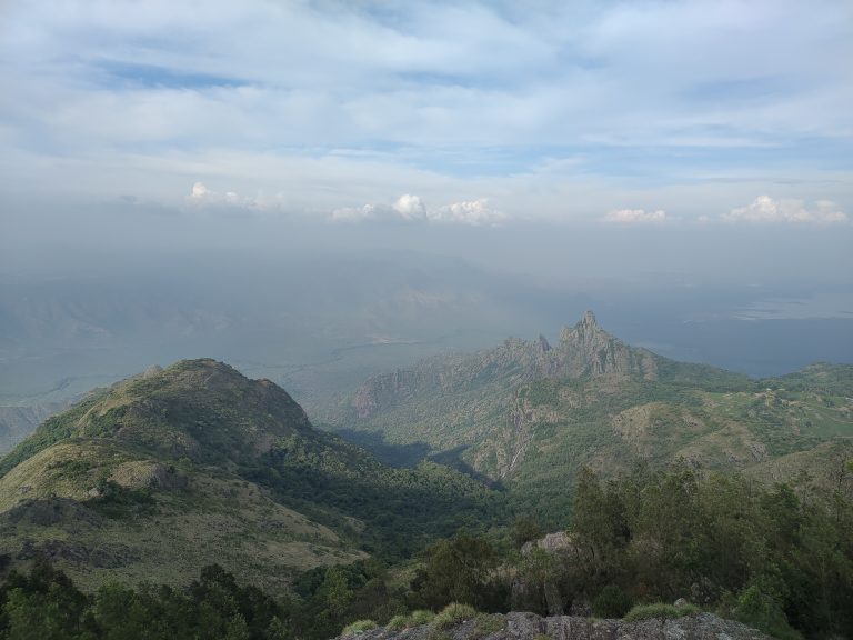 Looking down a mountain into a valley. There is a cloudy sky.