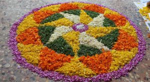 Circular design made from brightly coloured, flower petals arranged on a patterned tiled floor. This is known as an Onam Pookkala. 