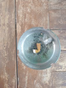 Small piece of a cigarette in an blue and grey ashtray, sat on a wooden table.
