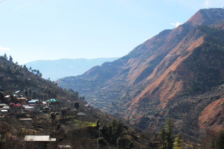 A village on the side of a mountain. Power lines run through the valley.