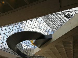 A spiral staircase leading upwards inside a glass pyramid in the Louvre Museum. 

