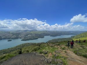 People standing on a grassy hillside looking out onto a lush mountainous, lake vista 