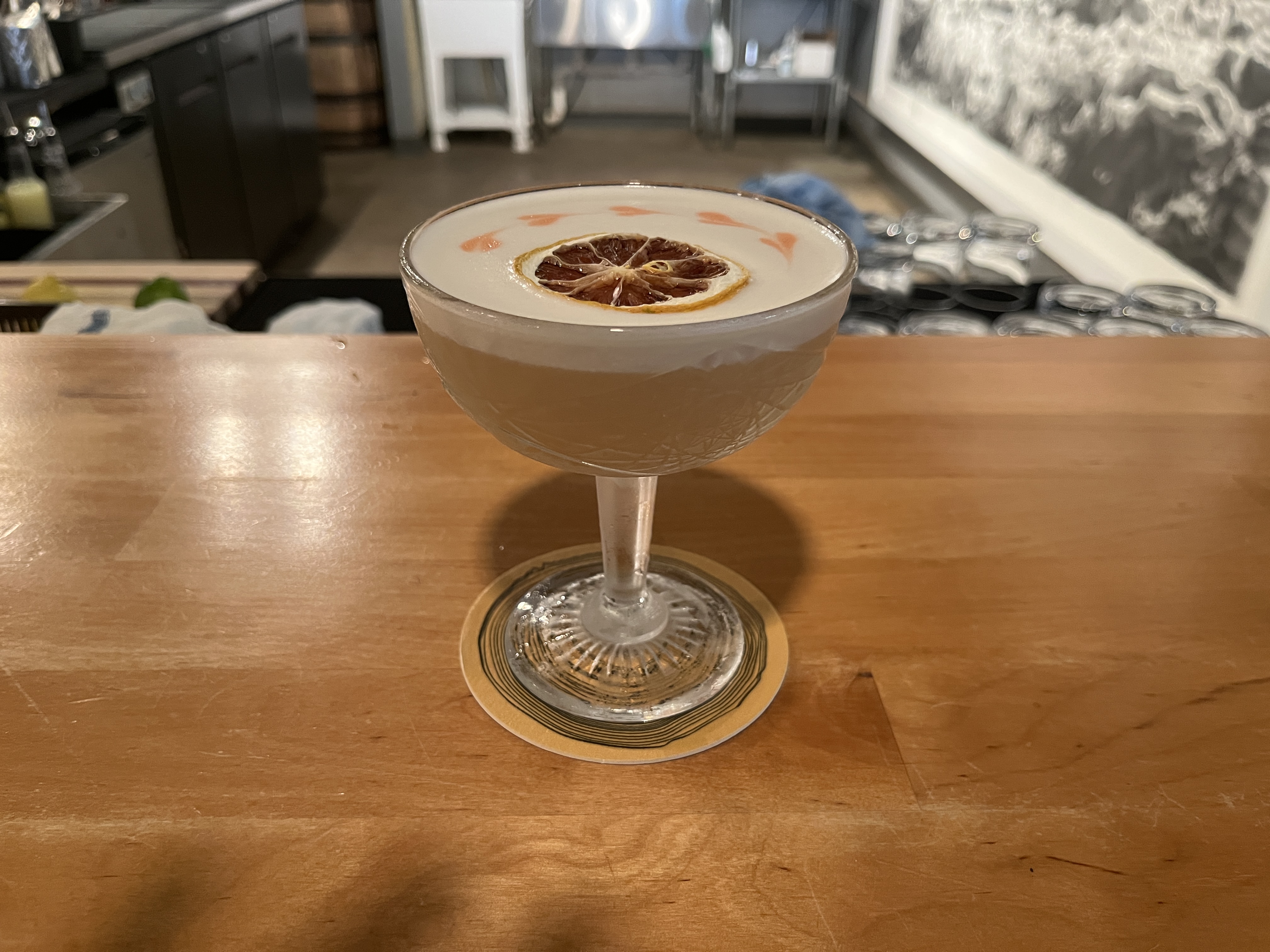 Whiskey sour cocktail. A coupe glass with a tall thin stem, a dried orange slice floating on top, decorated with bitters drops.