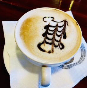 An example of Latte Art - a cup of milky, frothy coffee with a decorative pattern on top in a dark brown glaze effect. 