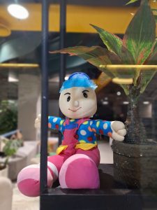 A doll sitting on a shelf beside a plant #WPPhotoFestival