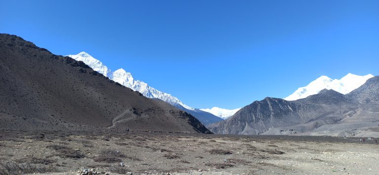 A landscape view of snow-capped mountains and neat and clean hills.