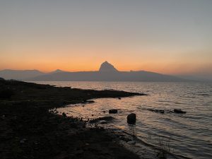 The sun setting over water with a mountain in the background
