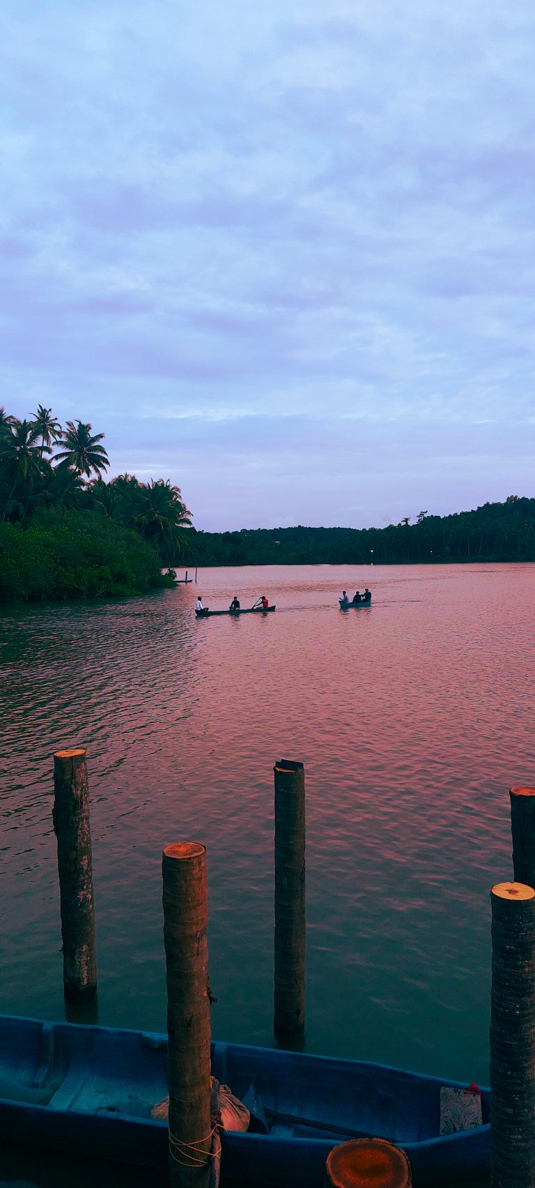 Tranquil river at sunset with boats and palm trees lining the shore.