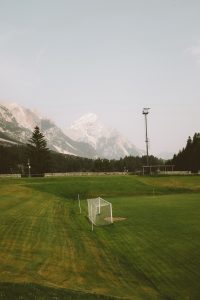 Soccer goal in view on a very green, open field with mountains and a cloudless blue sky in the background. 