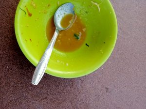 The food, possibly soup, has been consumed. A little remains in the bright green bowl along with the used spoon.
