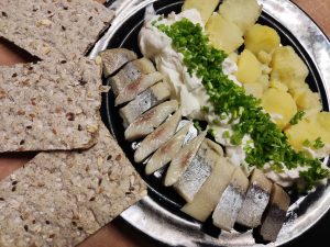 herring with potatoes and gzik (cottage cheese with cream) on a black plate

