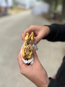 Street food sandwich in the foreground with hands holding it
