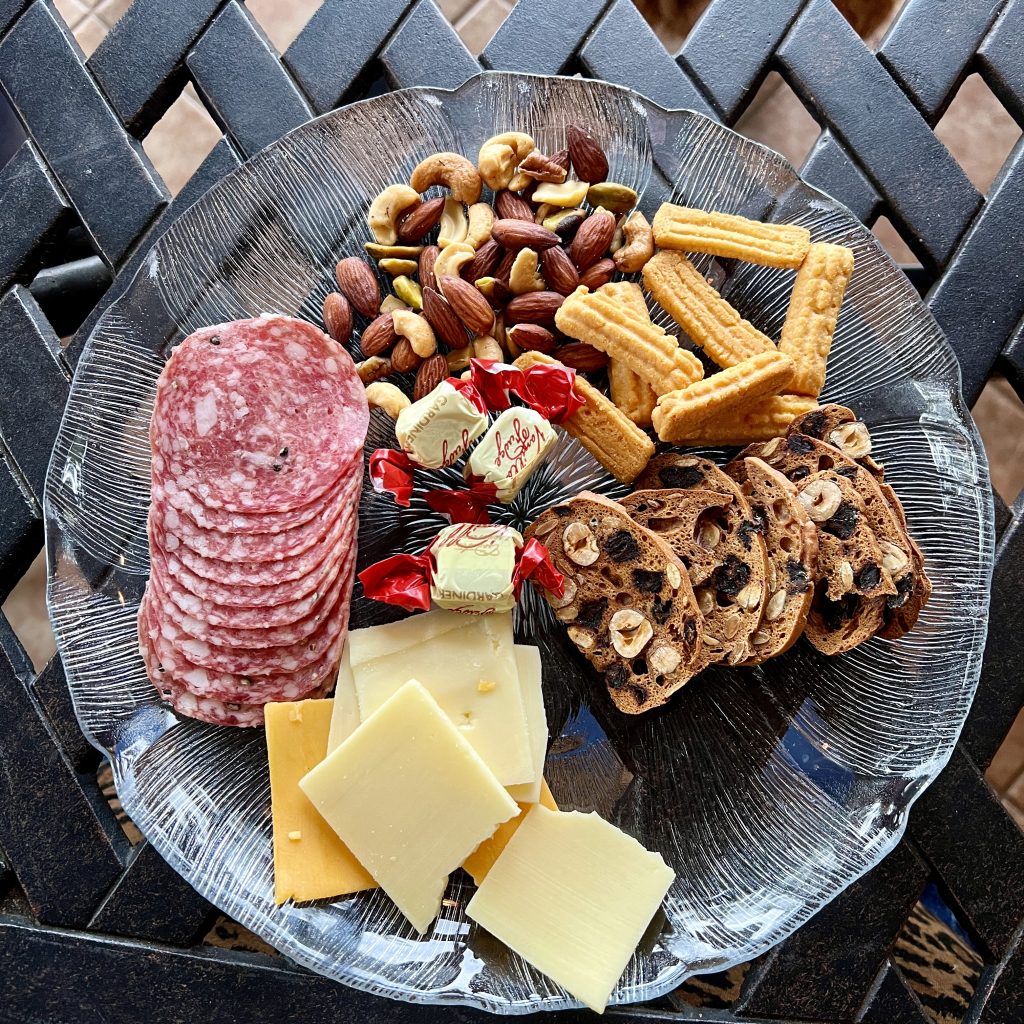 A charcuterie plate with mixed nuts, salami, wrapped candy, crackers, cheese, and biscuits.