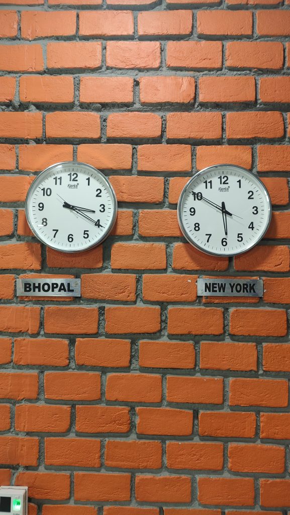 Clock on Wall with brick pattern. The bricks are painted in a vibrant orange color with gray mortar in between. Photo clicked at WordCamp Bhopal Contributor day Venue.