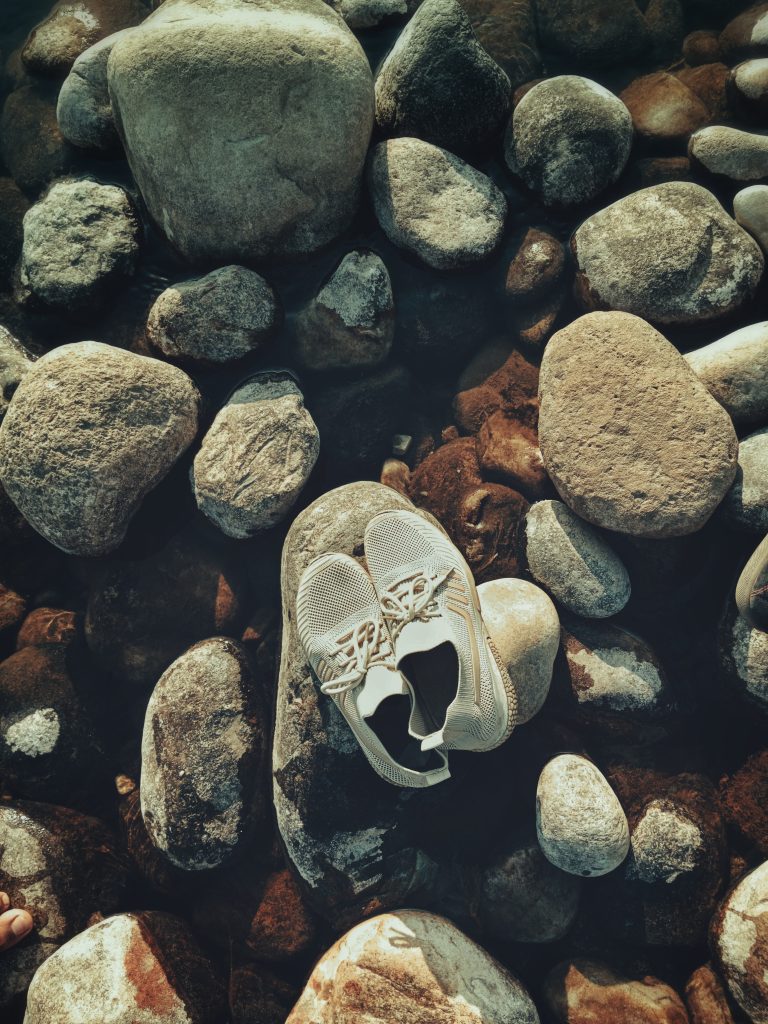 White tennis shoes placed on top of a pile of rocks rising above water.