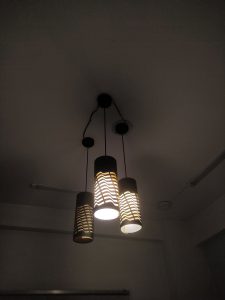 Three pendulum electric lights, with patterned lampshades, hanging from the ceiling of a dark room.
