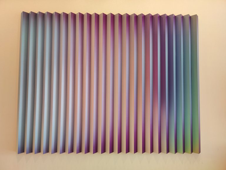 Vertical rectangular panels in gradient colors ranging from teal to purple, arranged side by side, against a light-colored wall.