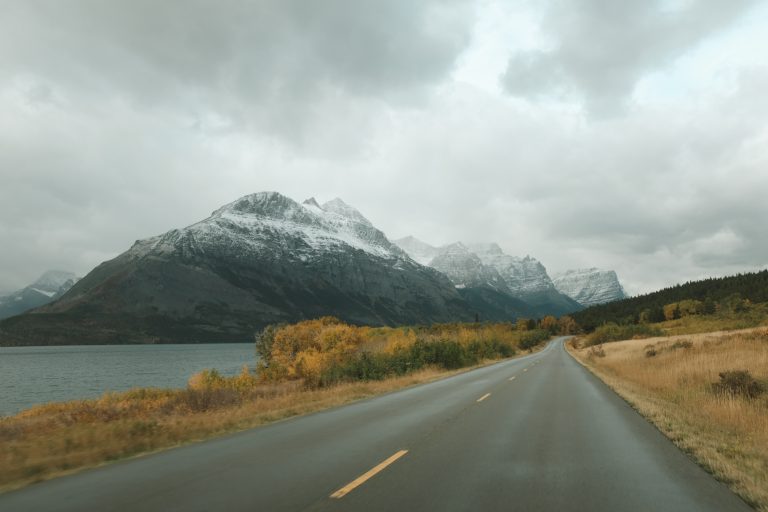 Road curving to the right with snowy mountains in the distance and yellow fall trees.