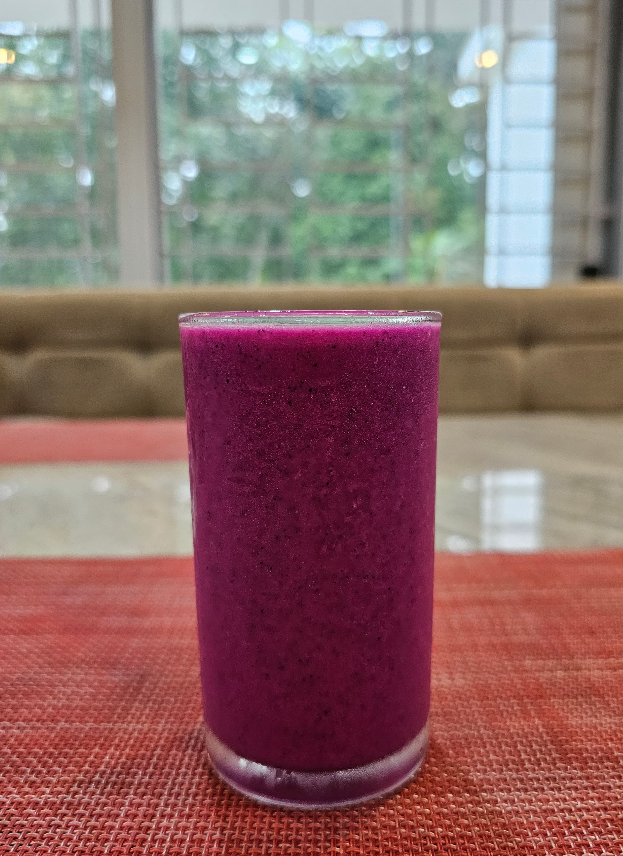 A frosted glass of Red Dragon Fruit milkshake on a table. 