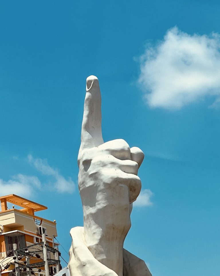 Sculpture of a human hand, pointer finger pointed at the sky.